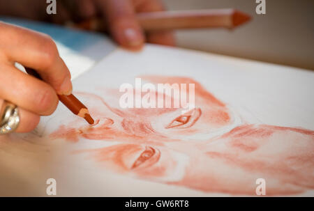 Young woman's hand making a pencil portrait, using the Sanguine (red chalk) technique. Stock Photo