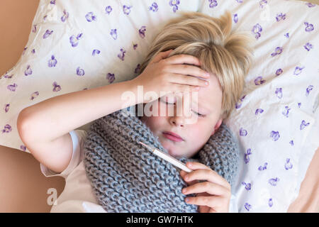 Sick little child boy holding thermometer laying in bed with sad face - healthcare and medicine concept Stock Photo
