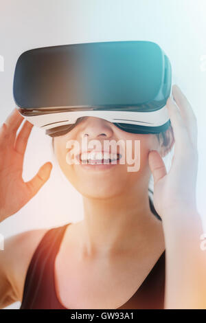 Close up shot of smiling young woman using the virtual reality headset against grey background with sunflare effect. Asian femal Stock Photo