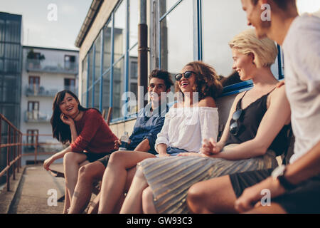 Multiracial group of friends sitting in balcony and smiling. Young people relaxing outdoors in terrace. Stock Photo