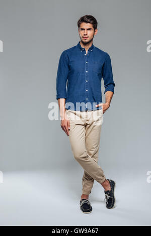 Full length portrait of a casual man standing with hand in pocket over gray background Stock Photo