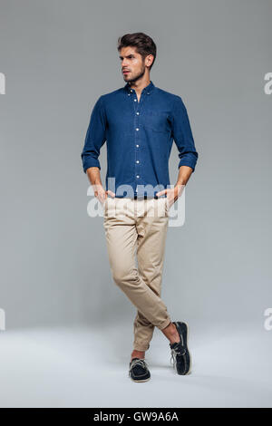 Portrait of a casual man standing with hands in pockets over gray background Stock Photo