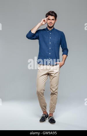 Full length portrait of a young man saluting isolated on a gray background Stock Photo