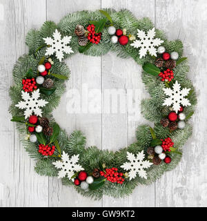 Christmas wreath decoration with white snowflake and silver and red bauble decorations, holly and snow covered blue spruce fir. Stock Photo