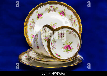 Antique fine china tea cups, saucers and cake plates on blue background. Stock Photo