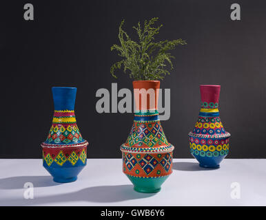 Still life of three artistic painted colorful handcrafted pottery vases and little green branches with harsh shadow Stock Photo