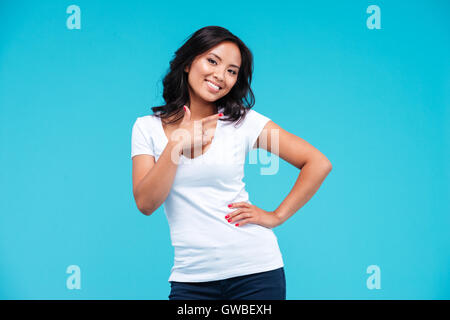 Smiling beautiful young vietnamese girl pointing finger away isolated on blue background Stock Photo