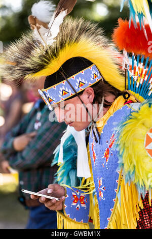 A Native American dancer from the Arapahoe people dressed in traditional costume checks his iPhone at the Indian Village during Cheyenne Frontier Days July 25, 2015 in Cheyenne, Wyoming. Frontier Days celebrates the cowboy traditions of the west with a rodeo, parade and fair. Stock Photo