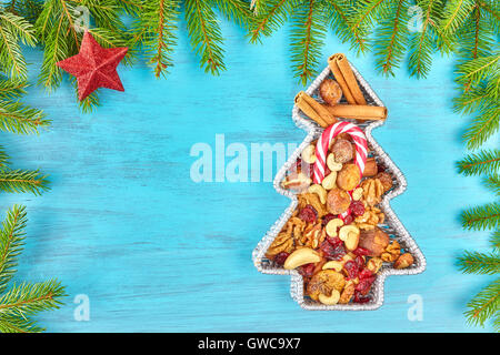 Christmas tree shaped container filled with nuts and dried fruits on a rustic wooden table, top view with copy space. Stock Photo