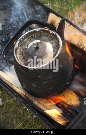 Old black boiling teapot on bonfire, vertical photo Stock Photo