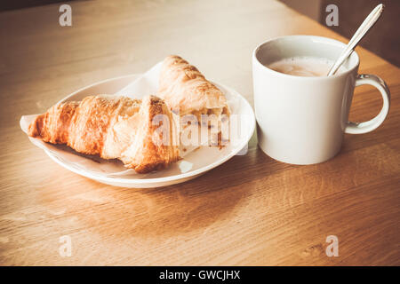 Cappuccino with croissant. White cup of coffee with milk foam stands on wooden table, closeup photo with soft selective focus Stock Photo