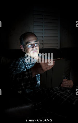 Middle aged man in pajamas reading tablet at night Stock Photo