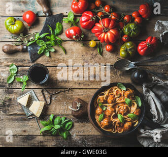 Italian pasta spaghetti with tomato sauce and meatballs in cast iron pan served with Parmesan cheese, fresh basil leaves and tom Stock Photo