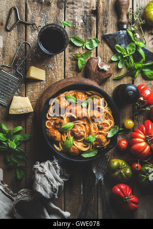 Italian pasta spaghetti with tomato sauce and meatballs in cast iron pan with Parmesan cheese, fresh basil, tomatoes and glass o Stock Photo