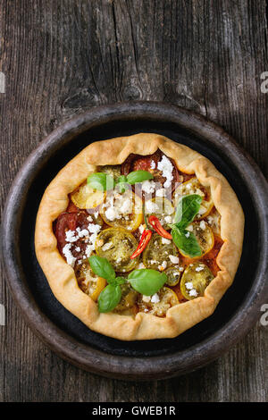 Homemade vegetable open pie galette with colorful tomatoes, tomato pesto, feta cheese and fresh basil, served in clay tray over Stock Photo