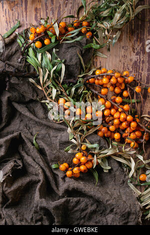 Ripe sea buckthorn berries on a branch with leaves on sackcloth rag over old wooden textured background. Top view Stock Photo