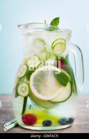 Infused water with cucumber, lemon, lime, berry and mint on blue background Stock Photo