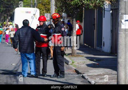 QUITO, ECUADOR - JULY 7, 2015: A man speaking with two firefighters on the street, people entering to pope Francisco mass Stock Photo
