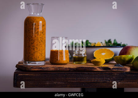 Turmeric Orange Poppy Seed Dressing in a bottle and a glass, served with a bowl of salad, halved oranges, an apple, turmeric and Stock Photo