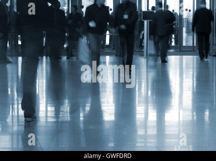 Blurred people silhouettes entering business center with glassy doors and reflections in the floor. Stock Photo