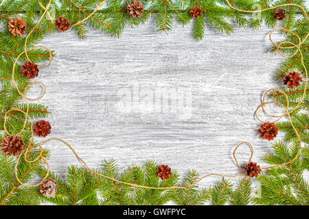 Christmas background, spruce branches frame with pine cones on a rustic wooden table, top view with copy space. Stock Photo