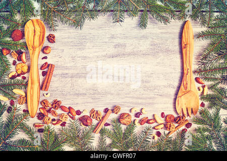 Retro toned Christmas background, spruce branches frame with wooden cutlery, nuts and dried fruits on a rustic table, top view w Stock Photo