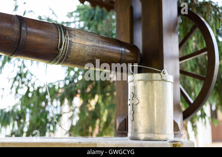 Ancient well with drinking water and a metal bucket with cross sign at Capriana Monastery in Moldova Stock Photo