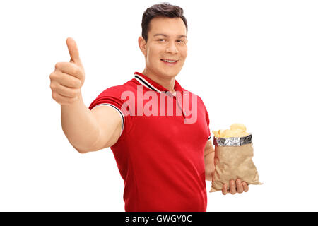 Smiling guy holding a bag of potato chips and giving a thumb up isolated on white background Stock Photo