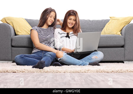 Two teenage girls sitting on the floor and looking at a laptop isolated on white background