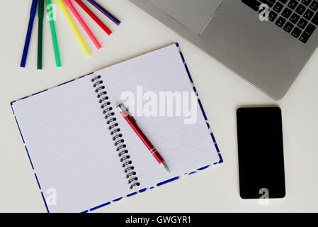 White desk with laptop keyboard, open notebook, colourful felt pens and mobile phone. Flat lay, top view Stock Photo