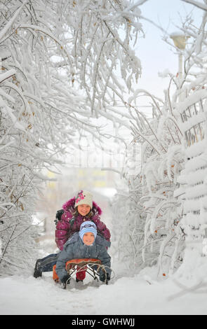 Two cute kids riding sled in winter time Stock Photo