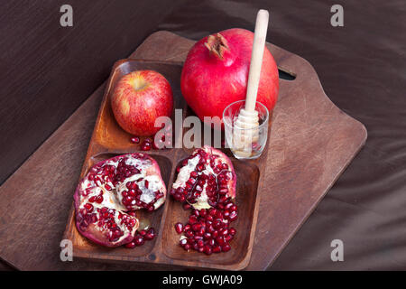 Pomegranates and apple with honey on wooden board