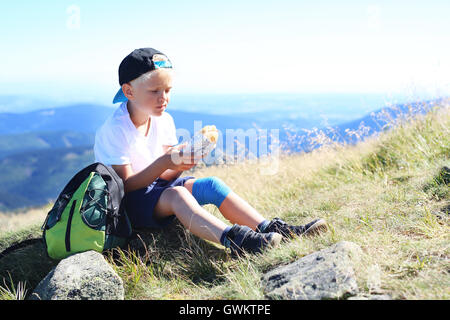 Vacation in the mountains. The child is eating a sandwich on a mountain trail Stock Photo