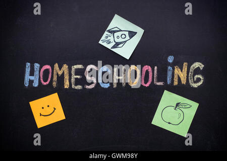 Homeschooling. Word Homeschooling writing on blackboard with paper notes with a rocket on it, apple and smile. Close up. Stock Photo