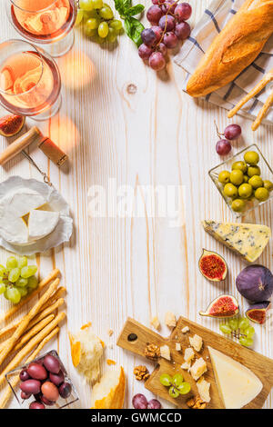 Different kinds of cheeses, wine, baguettes and fruits on white