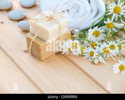 White rolled towel, soap bars tied with jute rope and chamomile bouquet on the natural wood planks background Stock Photo