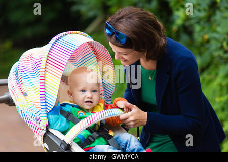 Young working mother and formal office outfit walking with her baby in colorful stroller. Mom and child in pushchair. Stock Photo