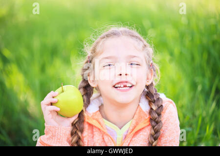 Sweet girl with a fallen tooth holding an apple in her hand on nature Stock Photo