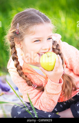 Little cute girl in the garden on a background of green grass with an apple in her hand Stock Photo