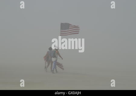 Burners carry a flag in a dust storm on the playa during the annual desert festival Burning Man September 1, 2016 in Black Rock City, Nevada. The annual festival attracts 70,000 attendees in one of the most remote and inhospitable deserts in America. Stock Photo