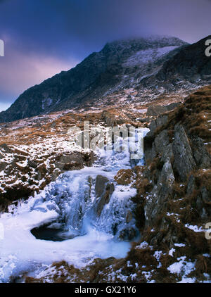 Small waterfall & partly frozen pool on a stream flowing down from Llyn Bochlwyd to Llyn Ogwen, Snowdonia, with Tryfan to rear. Stock Photo