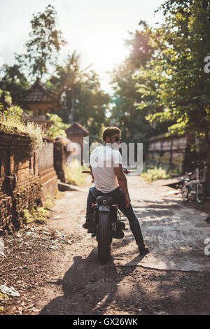 Outdoor shot of young man sitting on his motorcycle. Young male riding motorbike through a village. Stock Photo