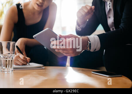Business colleagues working together in office, focus on man using electronic organizer in foreground and woman writing notes. Stock Photo