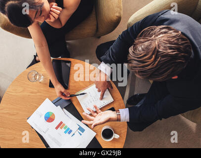 Overhead view of young businessman and woman looking at notepad while sitting at office lobby. Coworkers discussing new business Stock Photo