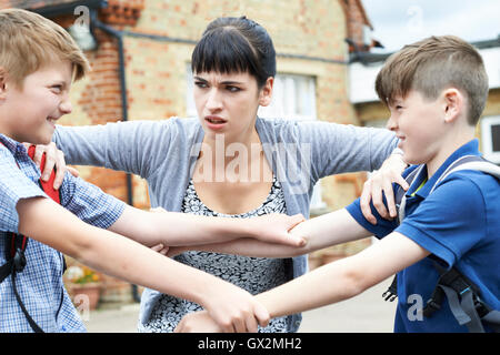 Teacher Stopping Two Boys Fighting In Playground Stock Photo