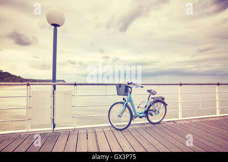 Vintage toned lonely bicycle with basket on empty pier, rainy summer day. Stock Photo