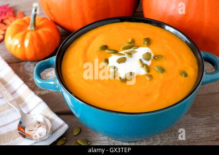 Creamy pumpkin soup topped with pumpkin seeds and cream in a blue bowl close up Stock Photo