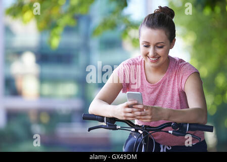 Young Woman Using Mobile Phone Whilst Out On Cycle Ride Stock Photo