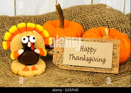 Happy Thanksgiving tag with turkey shaped cookie and pumpkins with burlap and wood background Stock Photo