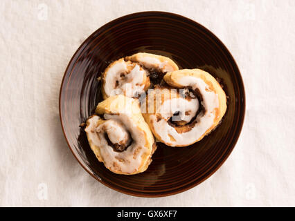 Freshly home baked and iced cinnamon scrolls on brown ceramic plate Stock Photo